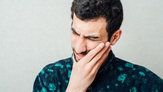 Mann med smerter, som holder seg på kinnet