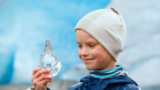 En gutt med lue kikker på en isbit han holder i hånda.