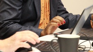 skriver på laptop, kaffekopp, papirer