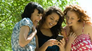 Tre venninner ser på noe morsomt på en mobiltelefon