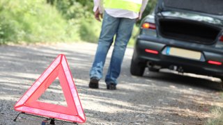 Varseltrekant ved vei der bil og person har stanset